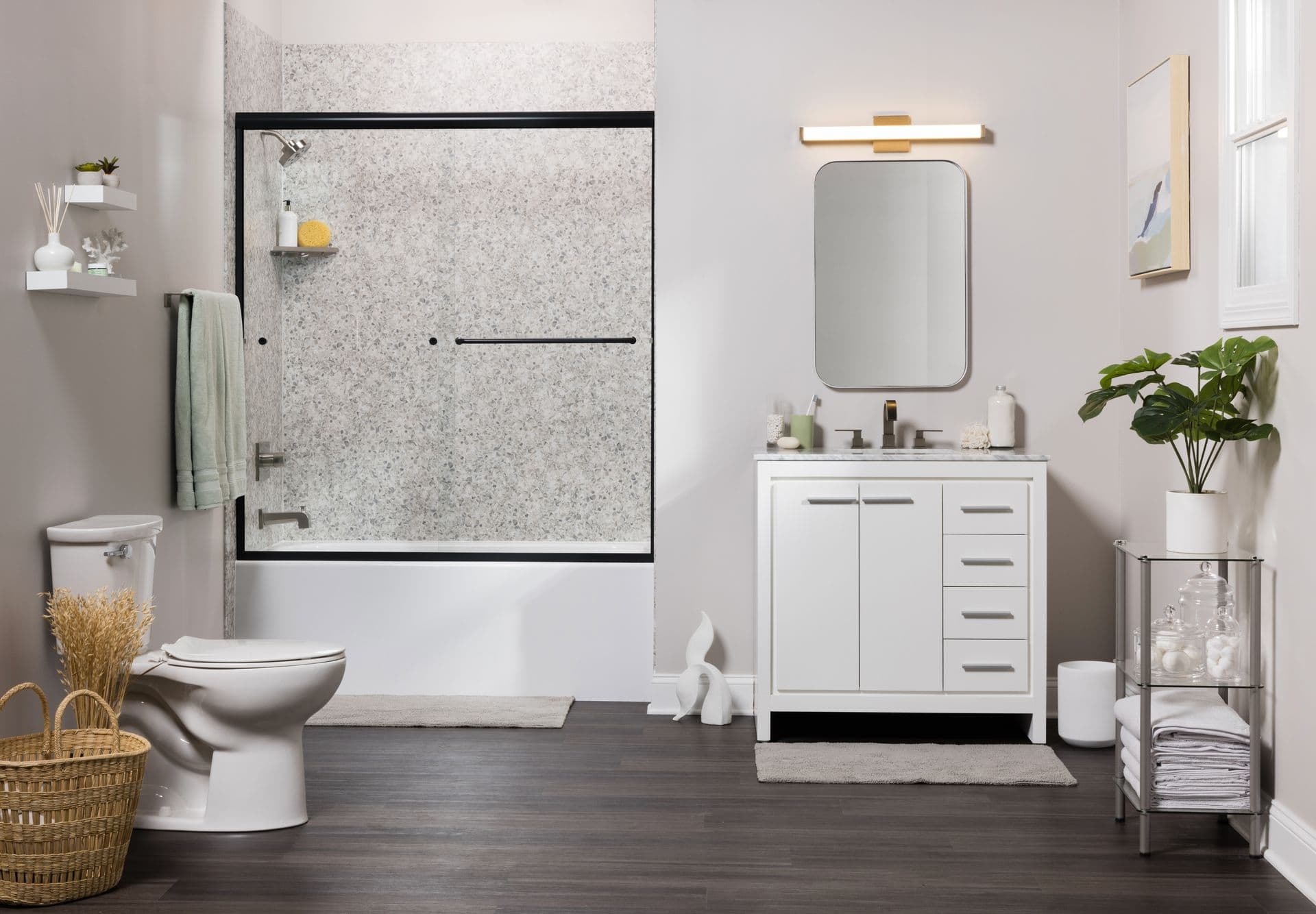 Bright bathroom with a white vanity and tub-shower combination featuring a speckled stone-look wall surround and black-framed glass doors.