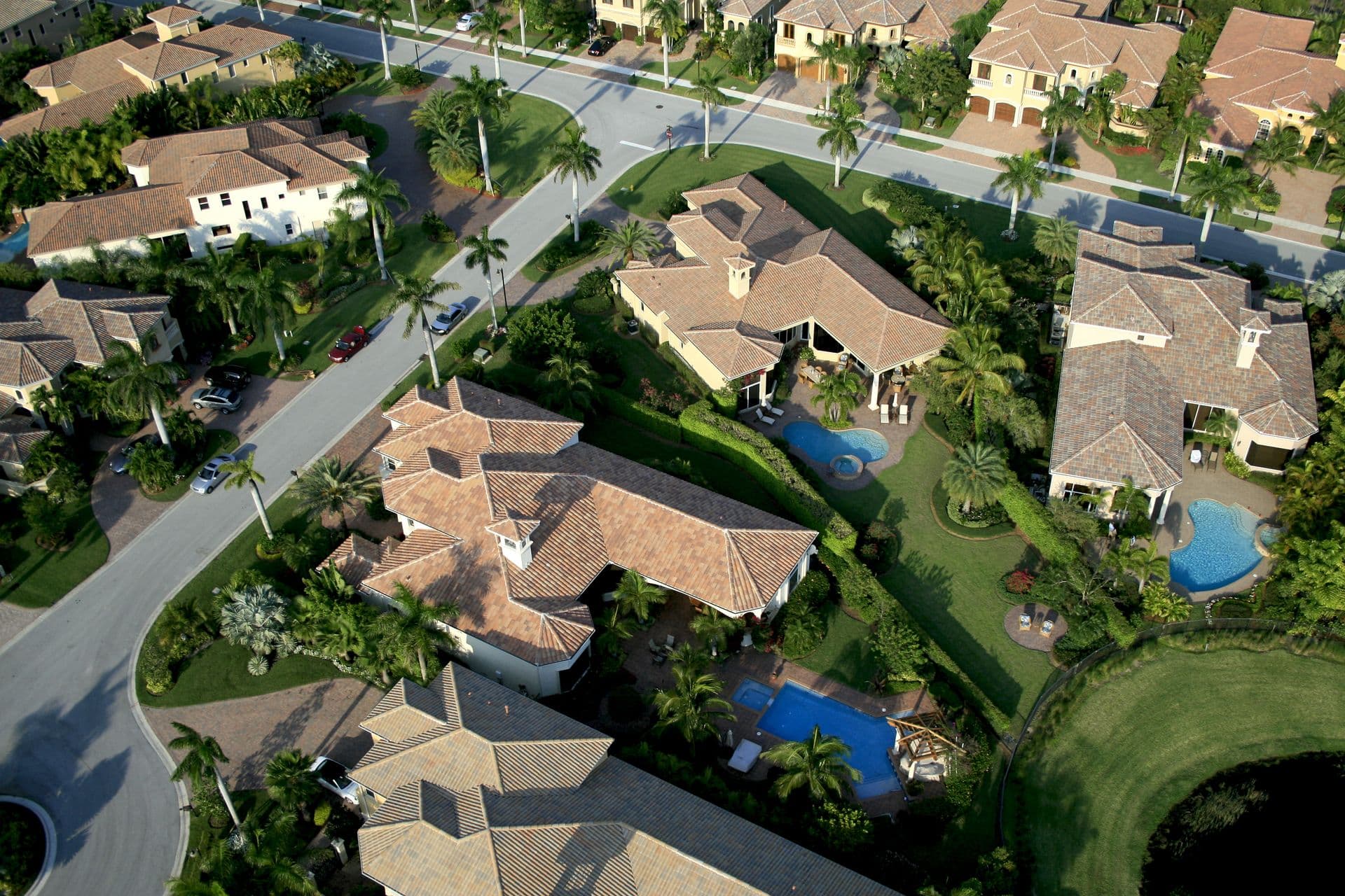 Aerial view of a palm-lined Florida residential neighborhood featuring upscale homes, lush landscaping, private pools, and well-maintained streets in a sunny suburban community.