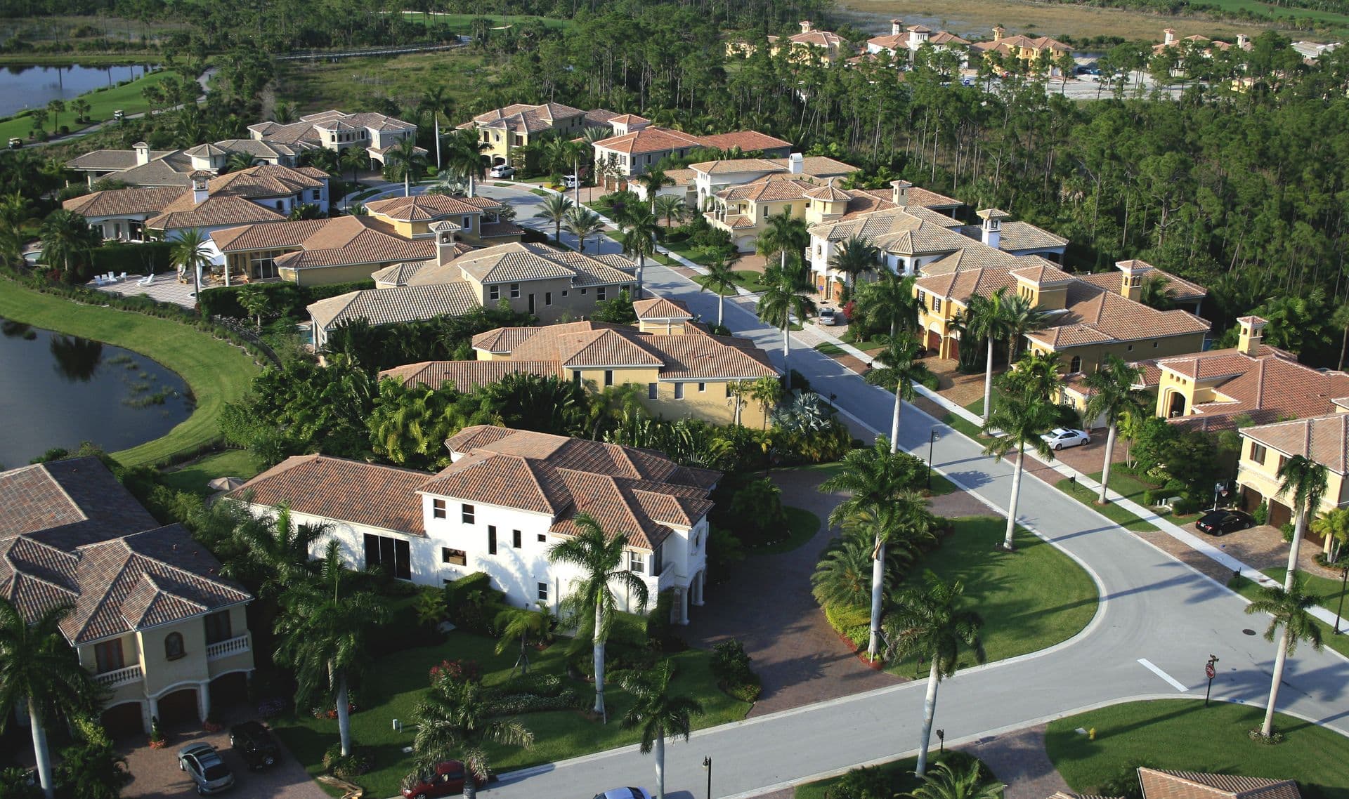 Aerial view of a luxury Florida residential community featuring Mediterranean-style homes with tile roofs, palm tree-lined streets, manicured landscaping, lakes, and lush natural surroundings.